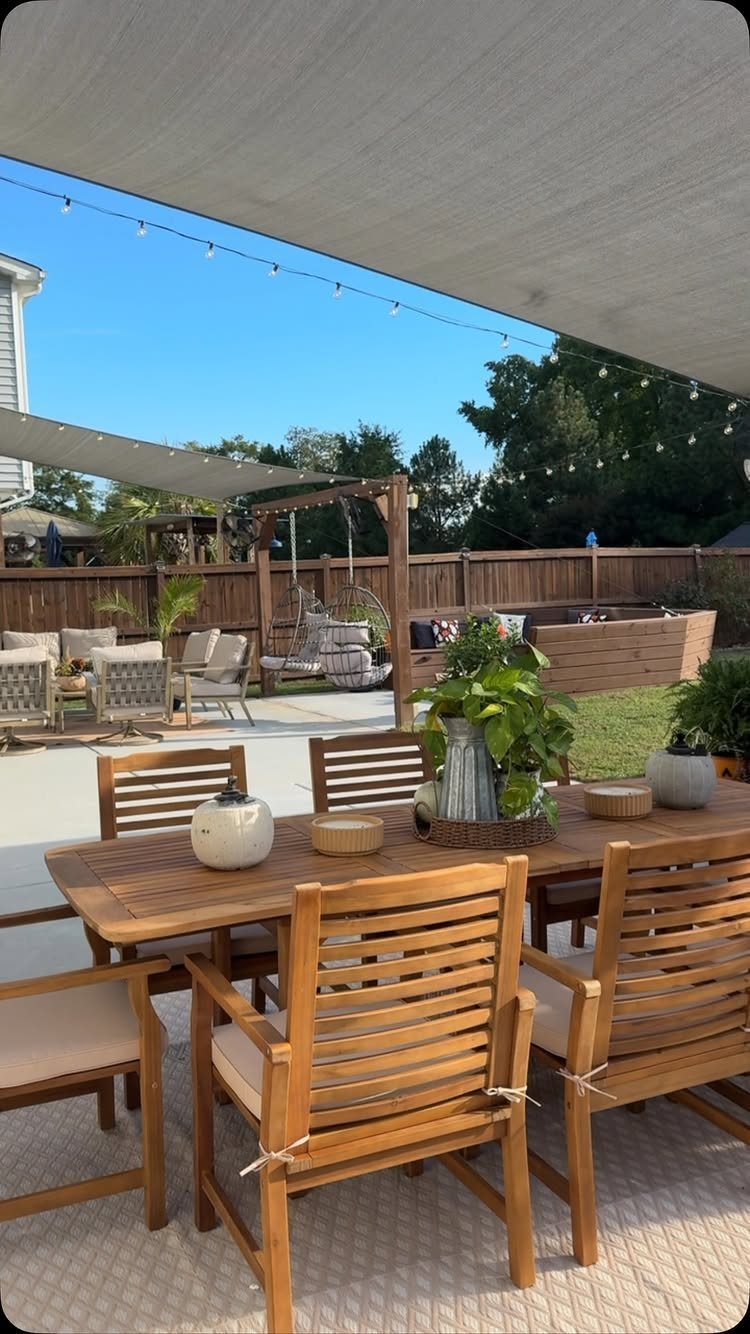 Wooden dining furniture on a patio with a swing set and lounge seating in the background.