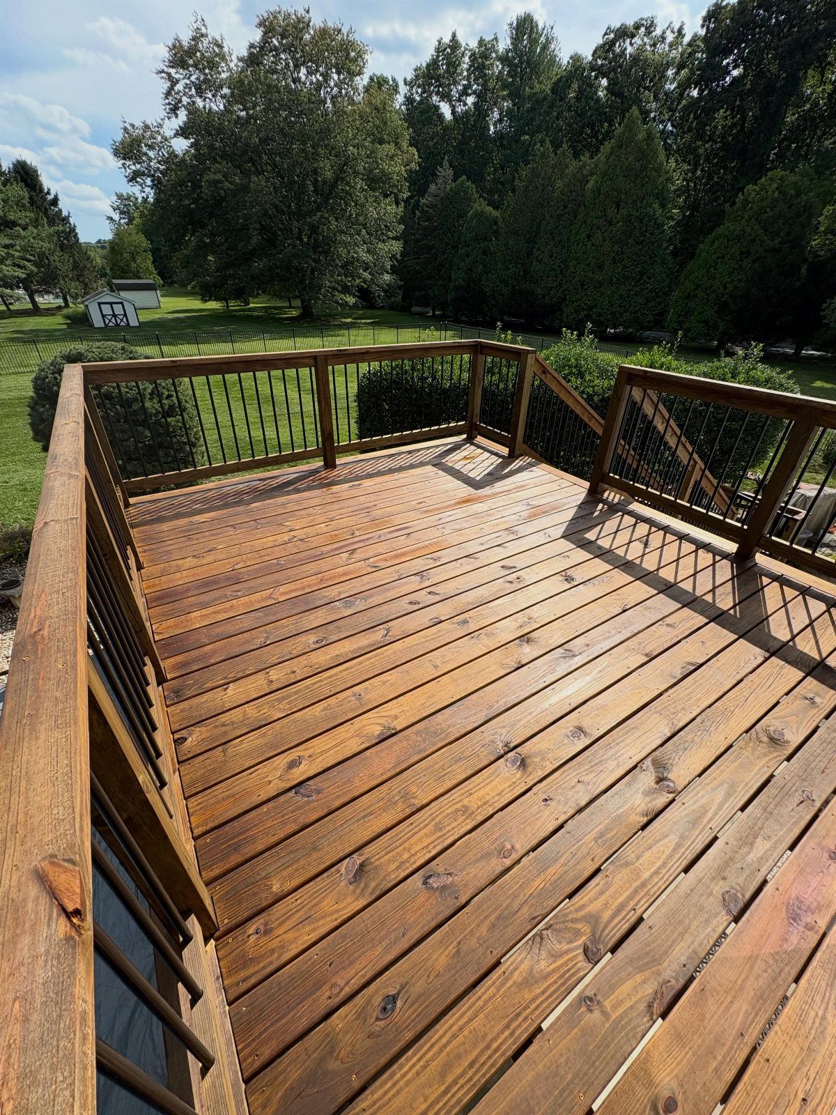 A cedar stained wooden deck with dark metal railings overlooking a green lawn and trees.
