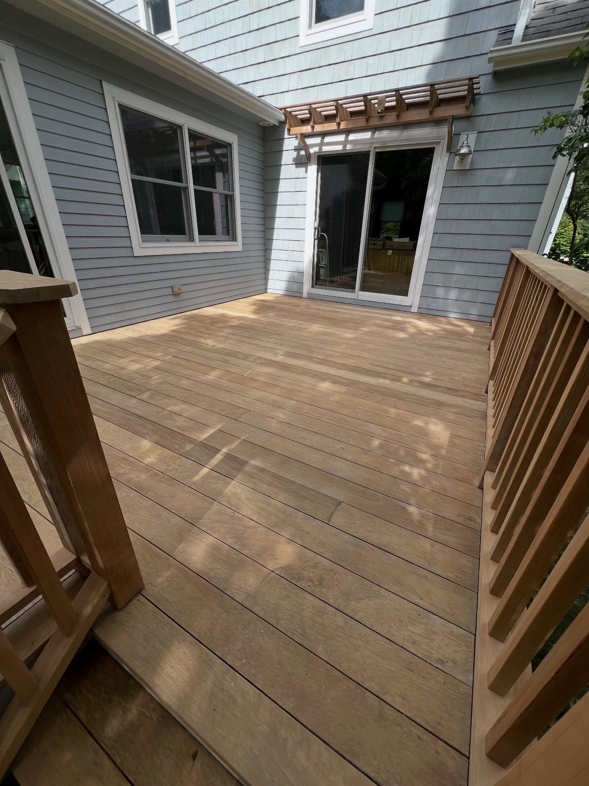 A light brown stained wooden deck attached to a blue house with white window frames.