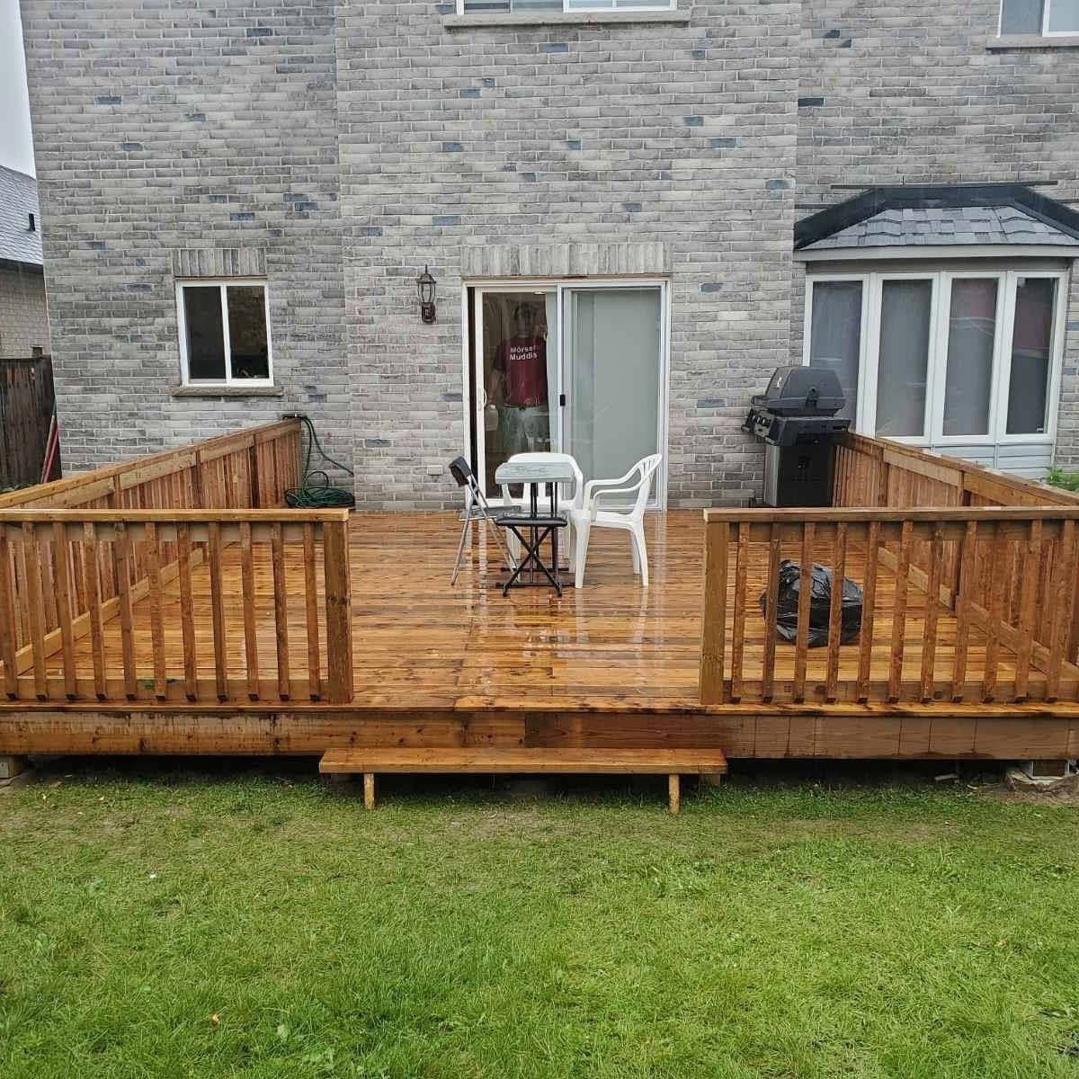 A large wooden deck with a warm honey-colored stain attached to a grey brick house.