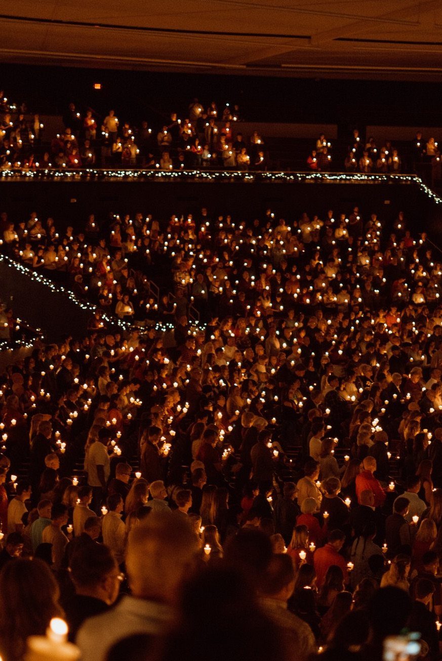 A large crowd of people holding glowing candles in a dark, multi-level indoor venue.