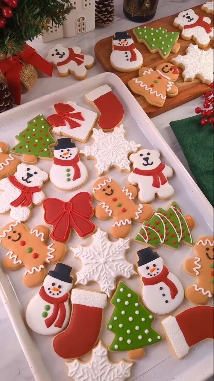 Decorated Christmas cookies in shapes of snowmen, gingerbread men, and trees on a white tray.