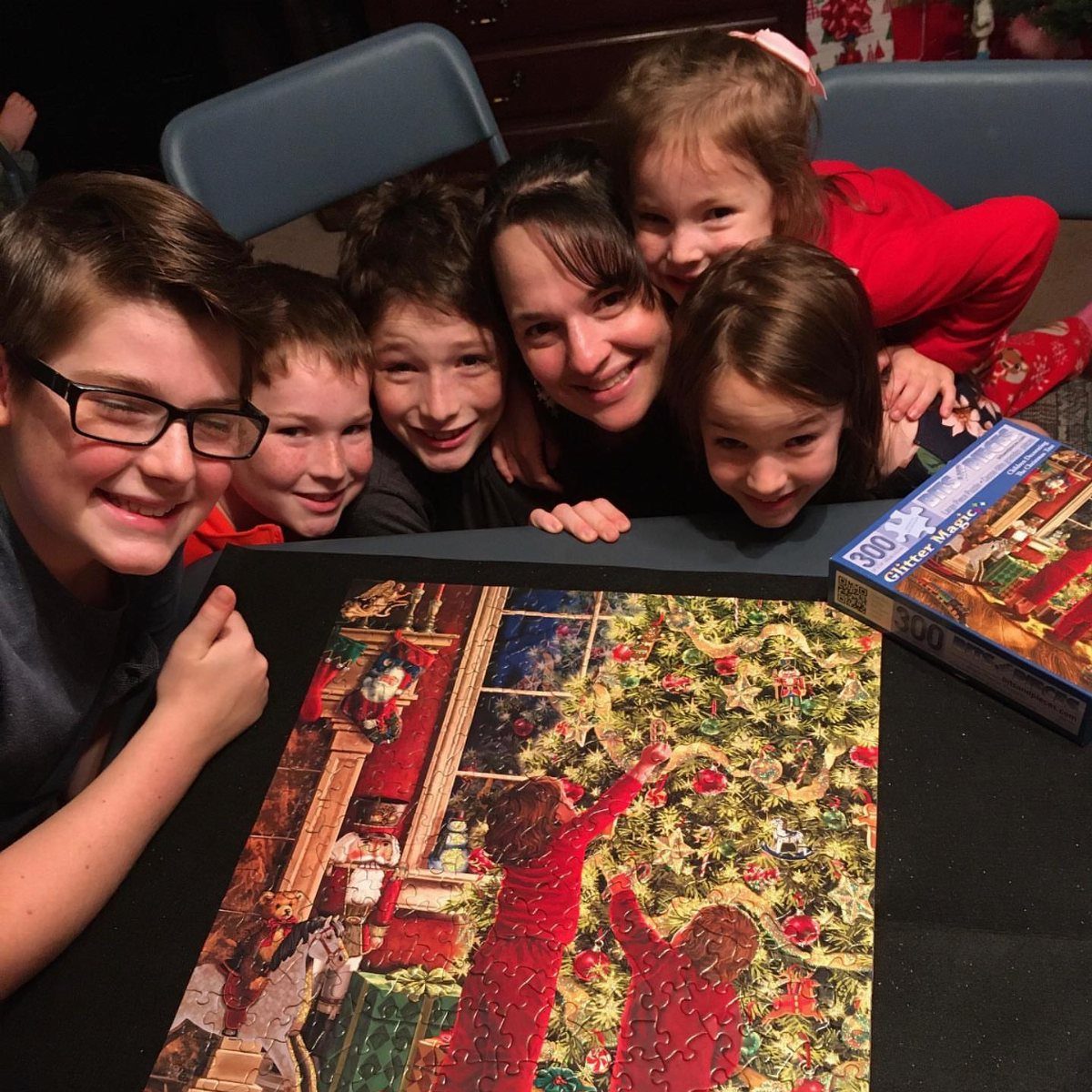 A smiling family poses behind a colorful Christmas jigsaw puzzle on a dark table.