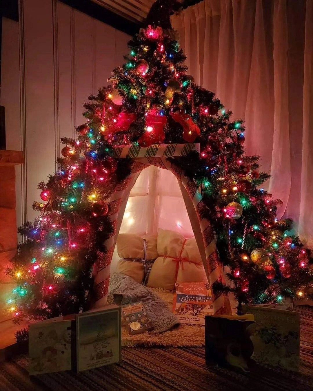A glowing Christmas tree fort made of branches and lights with pillows inside.
