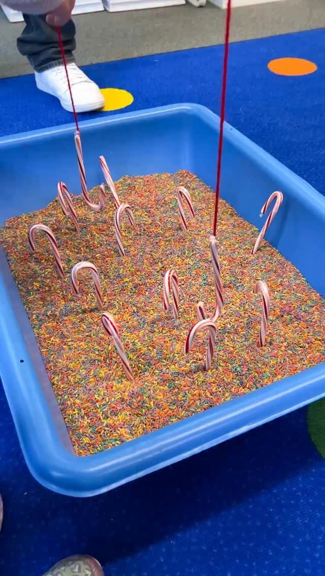 Candy canes stuck in colorful sprinkles inside a blue plastic bin during a sensory activity.