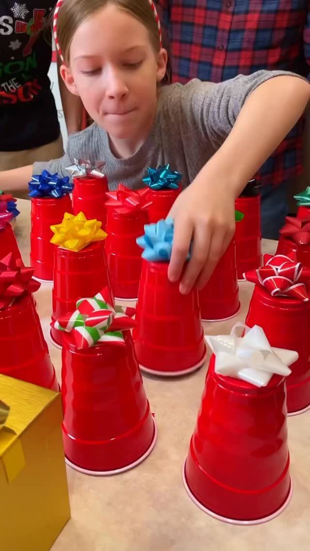 A young girl places colorful bows on top of red plastic cups to look like small gifts.
