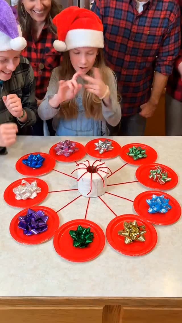Children in Santa hats look at a Christmas craft made of red plates and colorful bows.