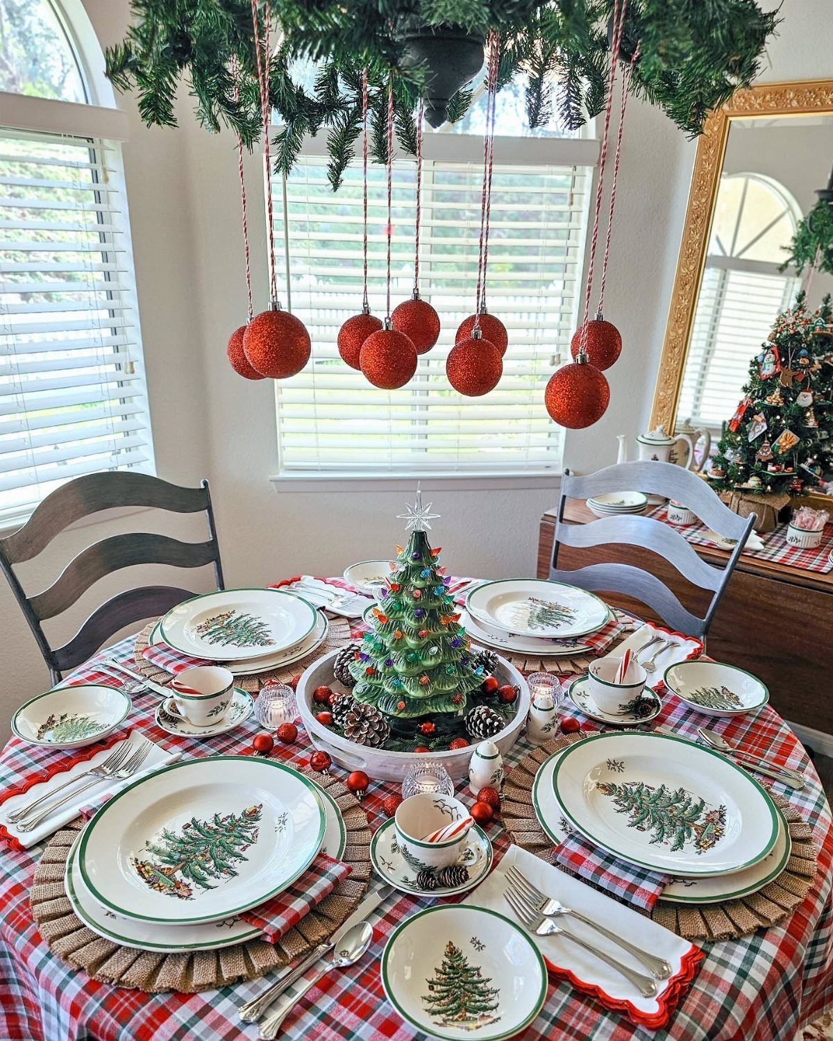 A festive Christmas table set with plaid tablecloth, themed plates, and a small decorated tree centerpiece.