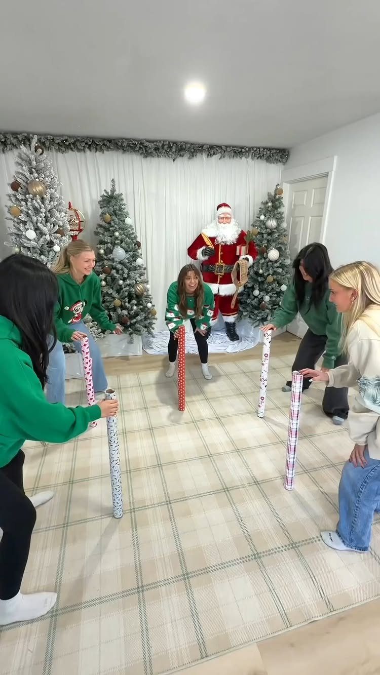 Young women in green sweatshirts playing a gift tube game in a Christmas decorated room.