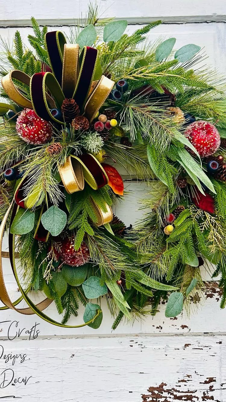A green Christmas wreath with gold ribbons and red beaded fruit ornaments on a white door.