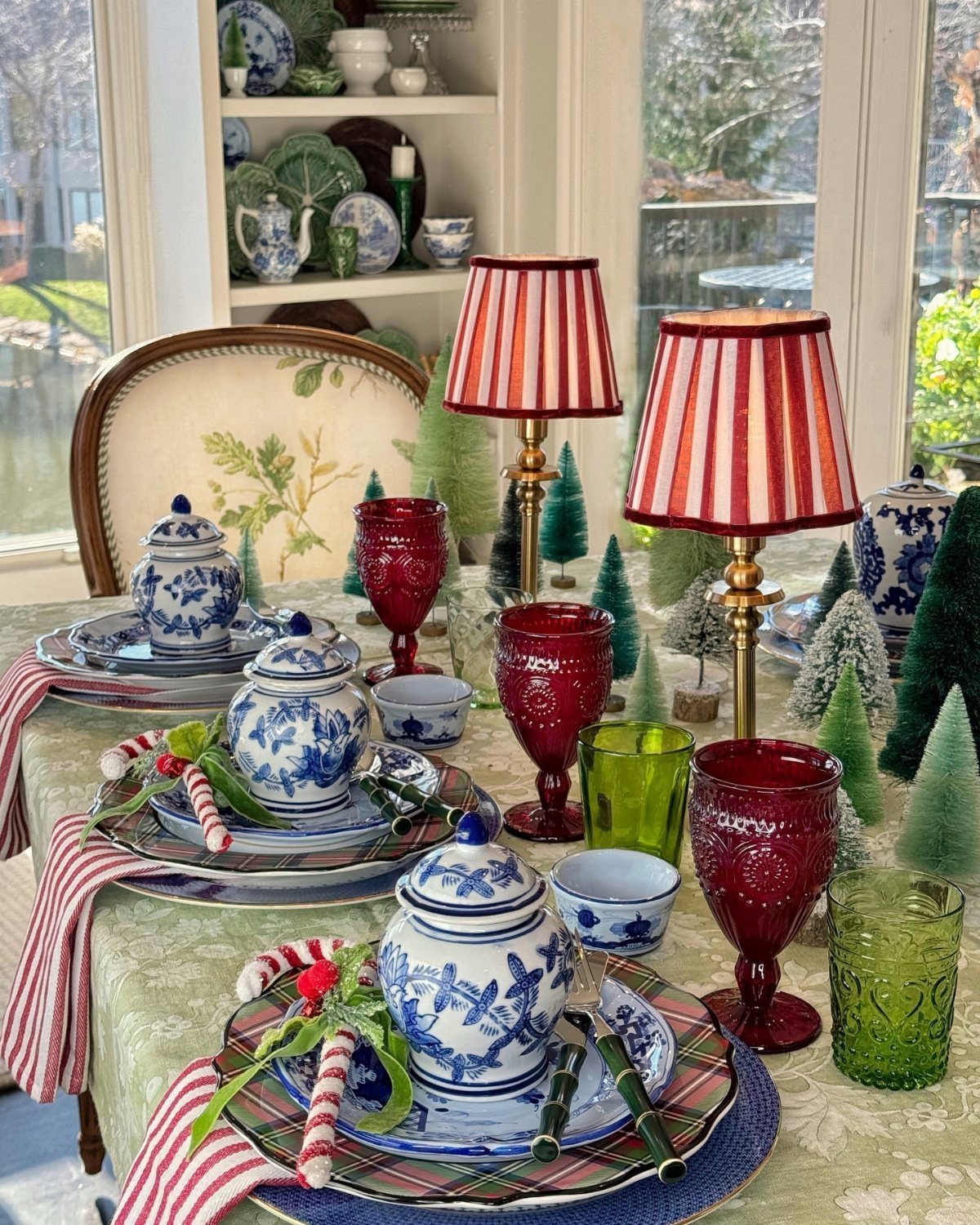 A festive dining table set with blue and white porcelain, red glassware, and small decorative trees.