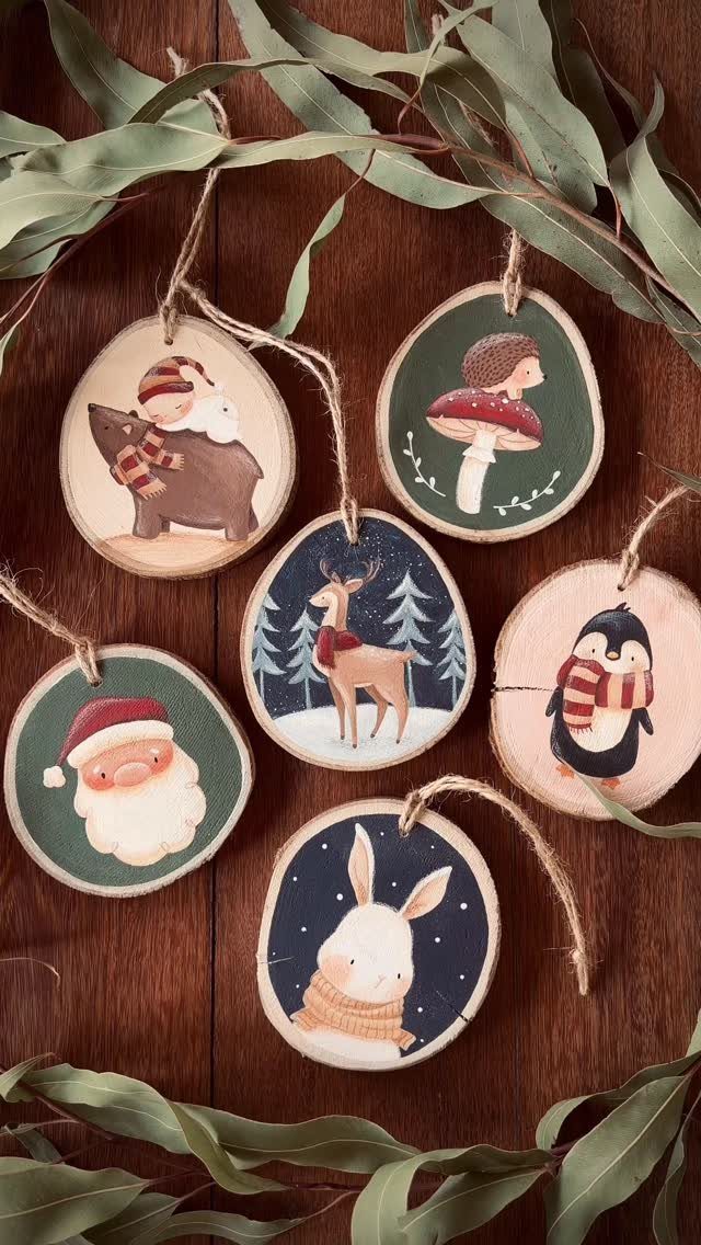 Six wooden slice ornaments with painted woodland animals and festive characters hanging on a wooden background.