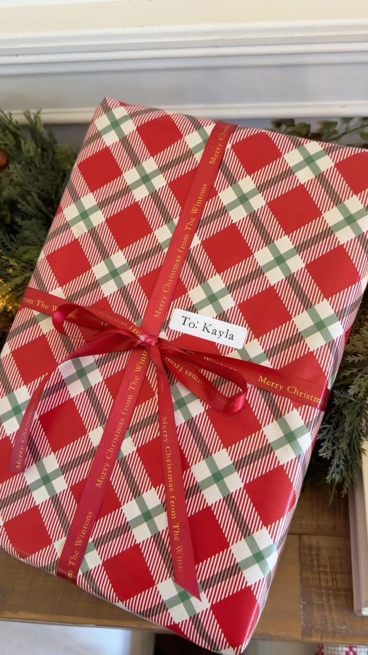 A gift wrapped in red and green plaid paper with a red ribbon and name tag.