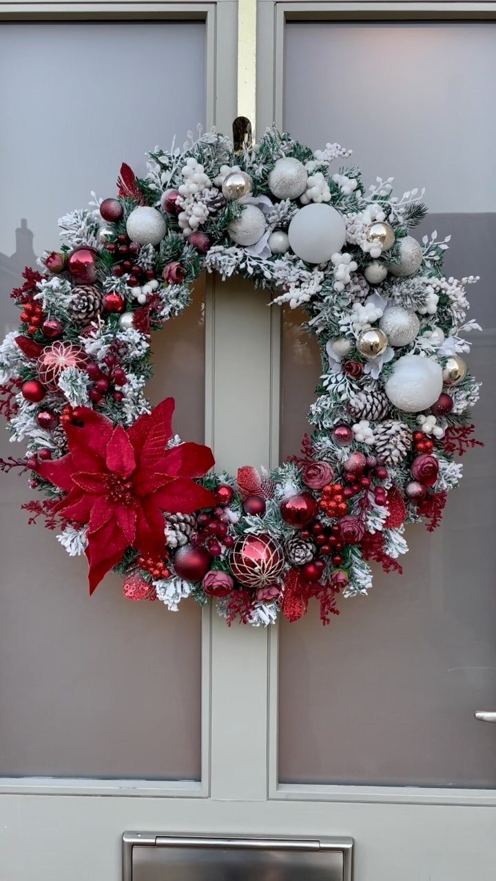 A large flocked Christmas wreath with red poinsettia and ornaments hanging on a door.