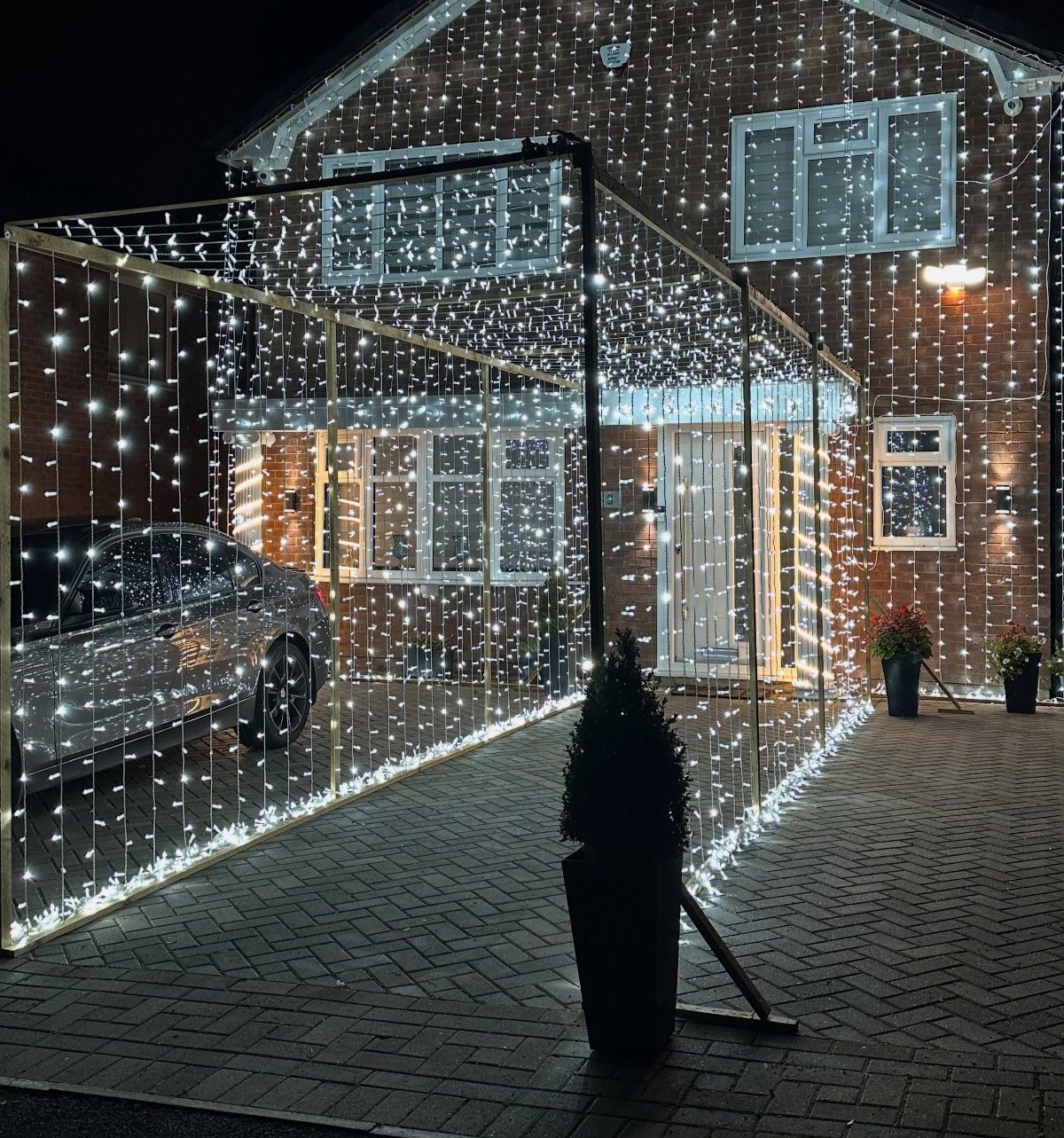 A driveway illuminated by a structure of hanging white fairy lights forming a tunnel.