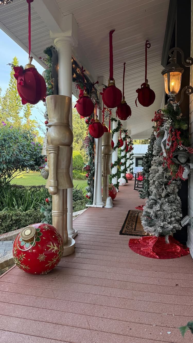 Red ornaments hang from a porch ceiling alongside a tall gold nutcracker statue and festive greenery.