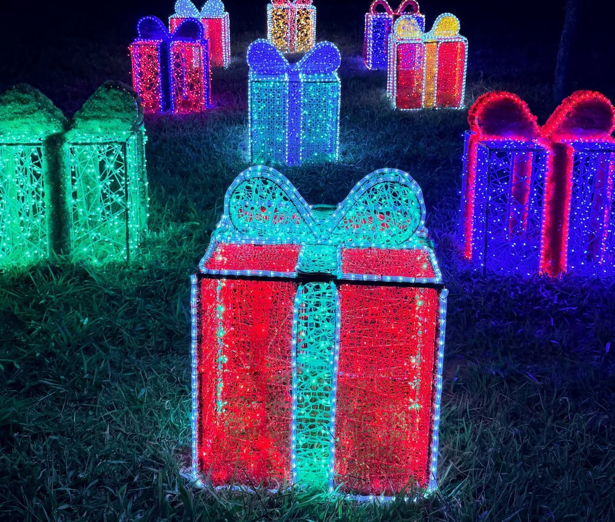 Large, colorful LED light gift box decorations scattered across a dark green grass lawn at night.