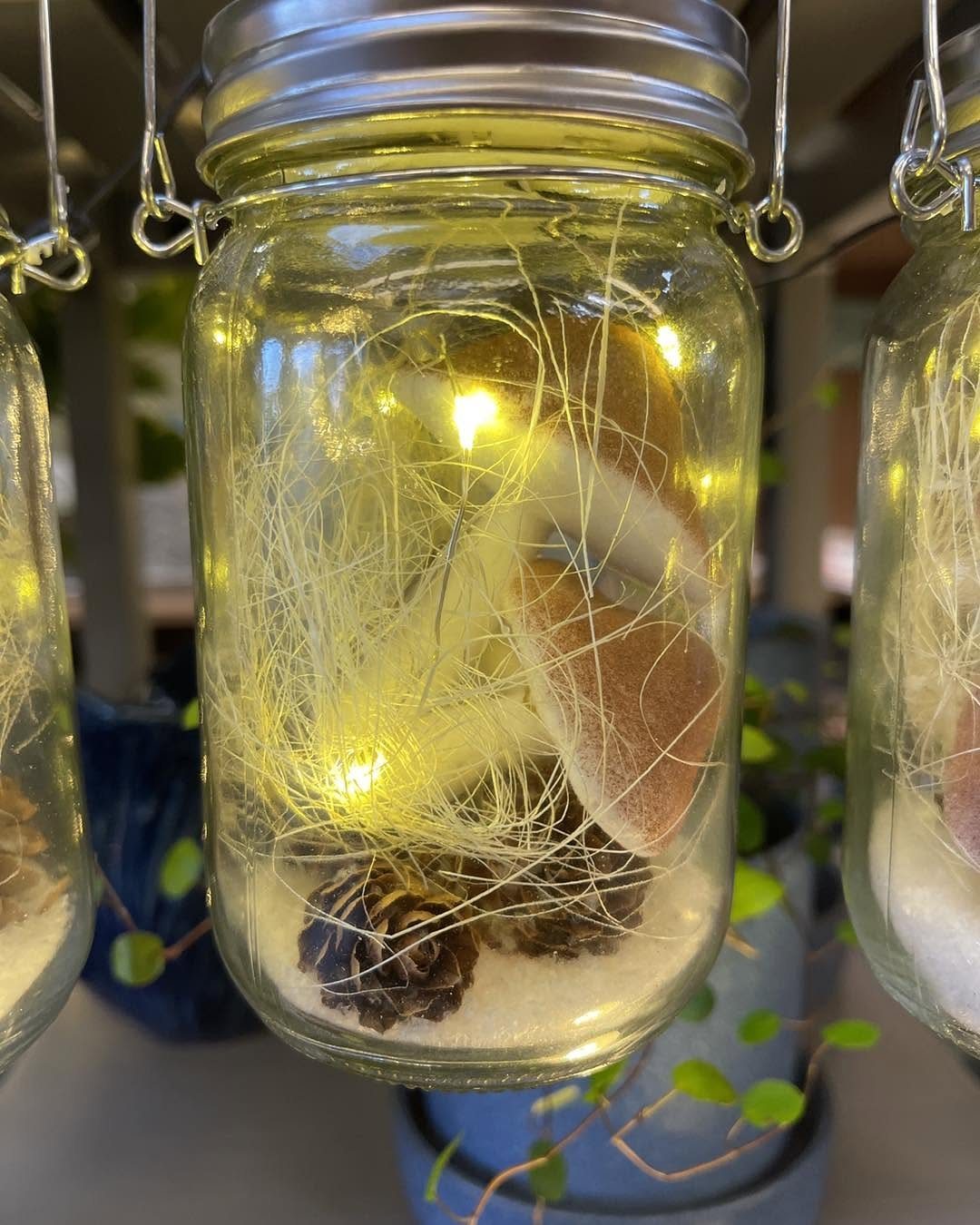 A hanging mason jar lantern filled with fairy lights, pine cones, and white decorative fibers.