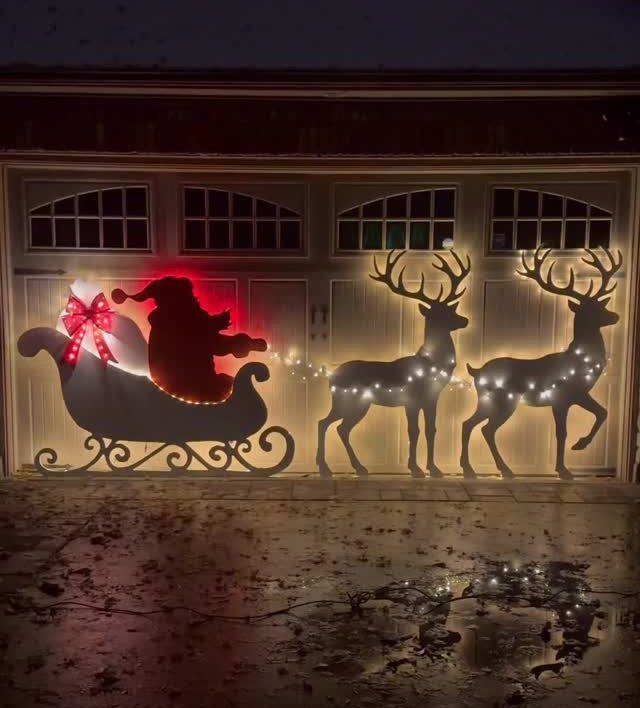 Lighted silhouettes of Santa in a sleigh and two reindeer decorating a driveway at night.