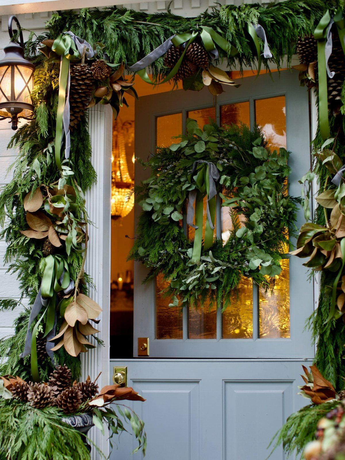 Evergreen garland with pine cones and ribbons decorating a light blue front door with a wreath.