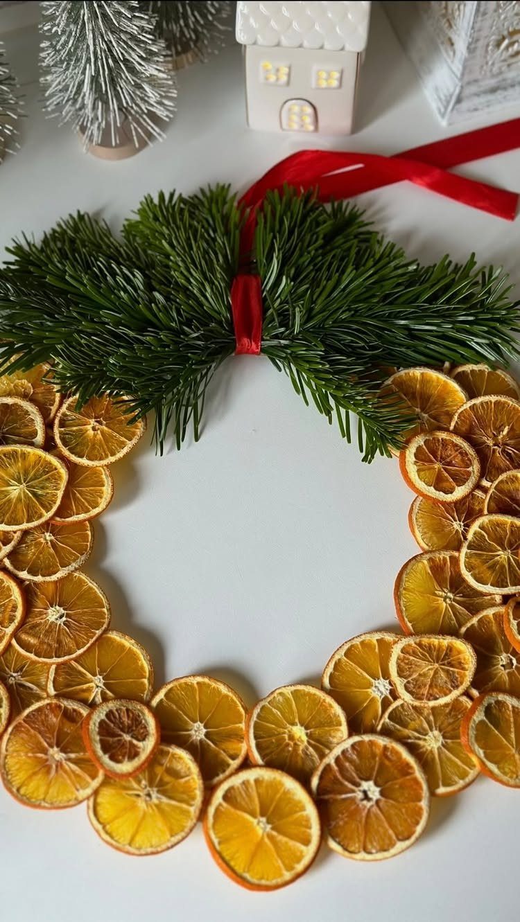 A wreath composed of dried orange slices and green pine needles tied with a red ribbon.