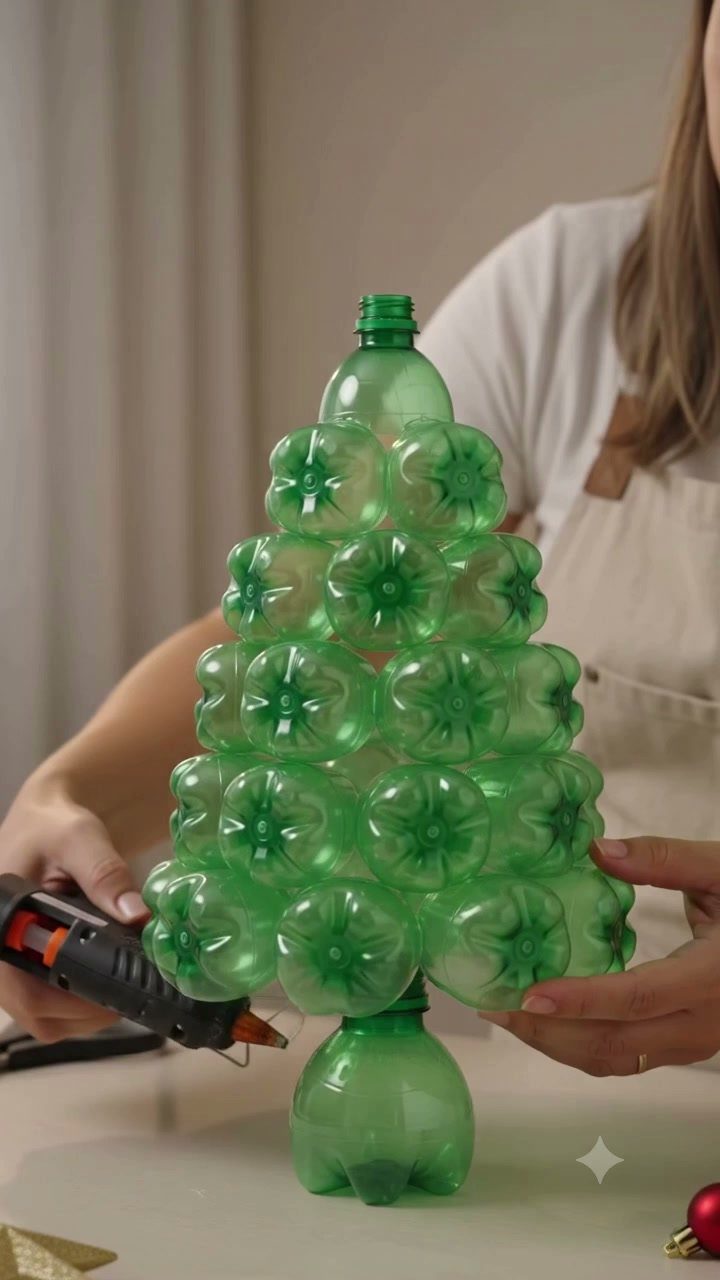 Christmas Tree DIY: 3 Ideas Using Wood, Paper and Plastic 3 A person assembling a green Christmas tree made from recycled plastic soda bottles using a glue gun.