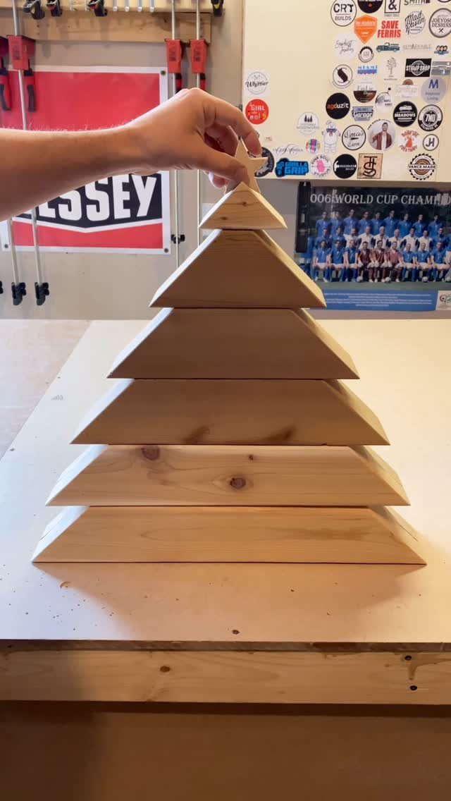 Christmas Tree DIY: 3 Ideas Using Wood, Paper and Plastic 1 A hand placing a wooden star atop a tiered pine wood Christmas tree on a workbench.