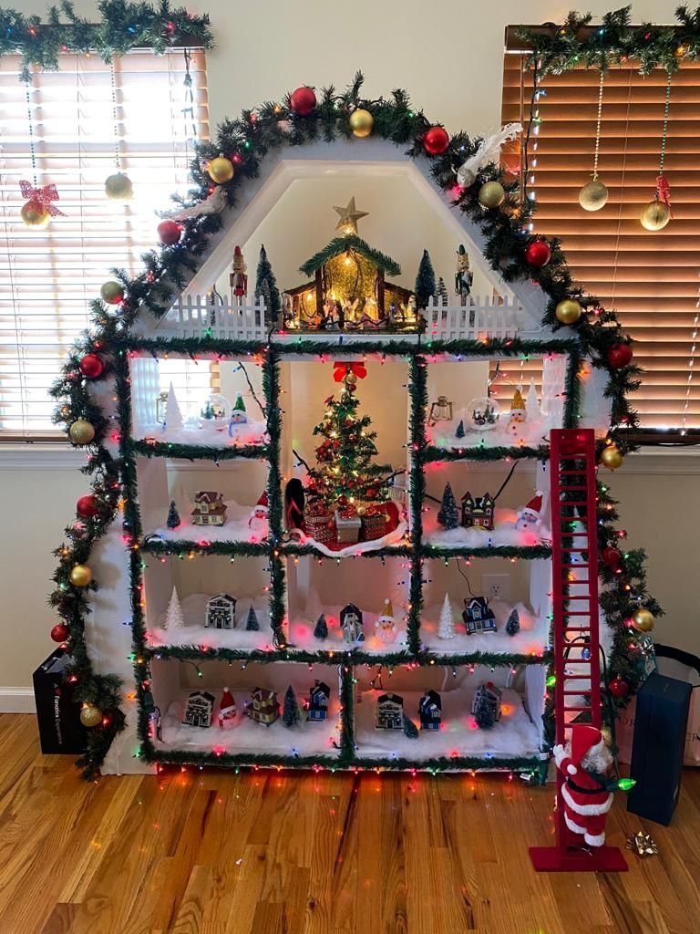 Christmas Tree Shelf: 6 Ideas from 2x4 Builds to Live Edge 5 A white house-shaped shelf displaying a miniature Christmas village with tiny buildings and festive lights.