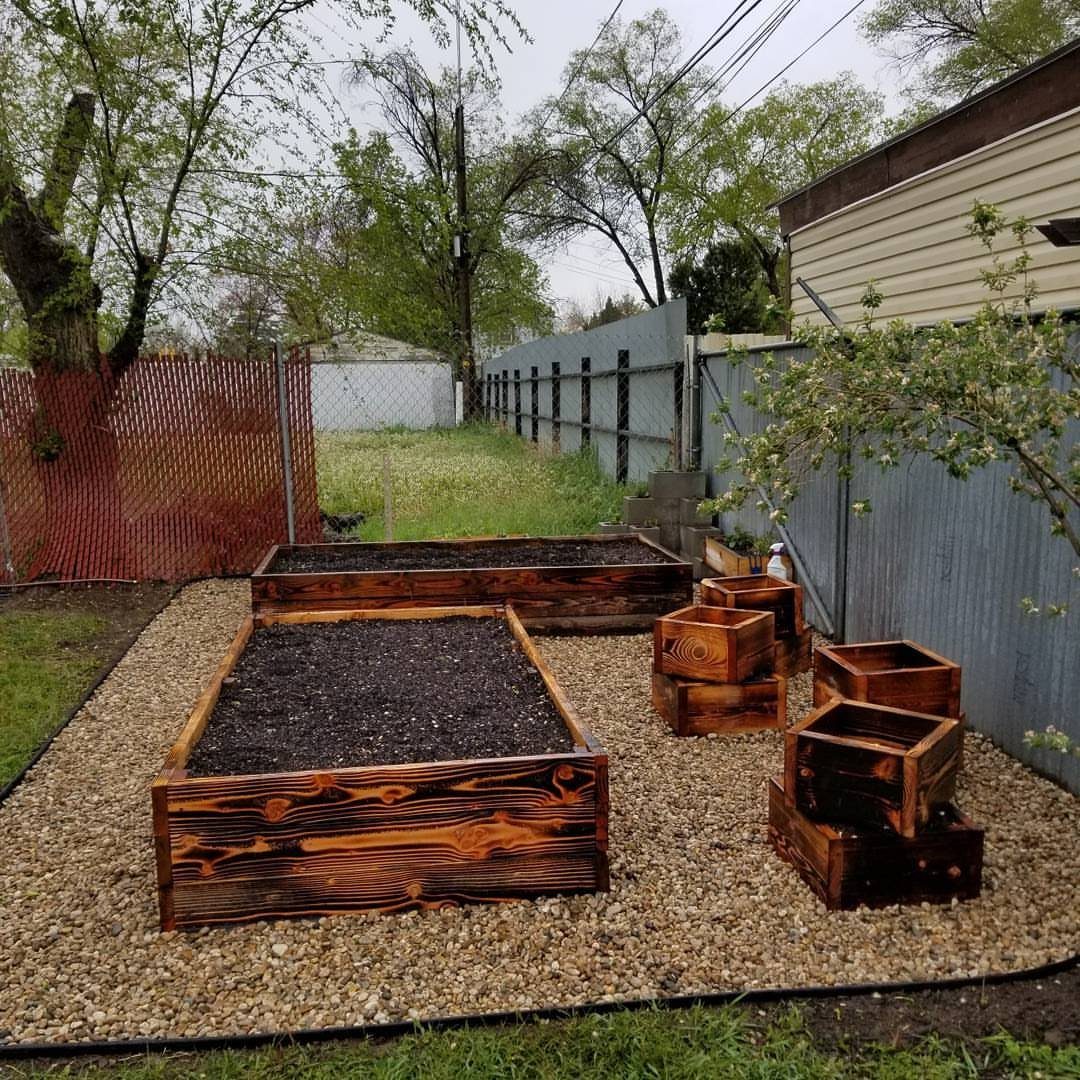 Wooden raised garden beds filled with soil sitting on gravel in a backyard corner.