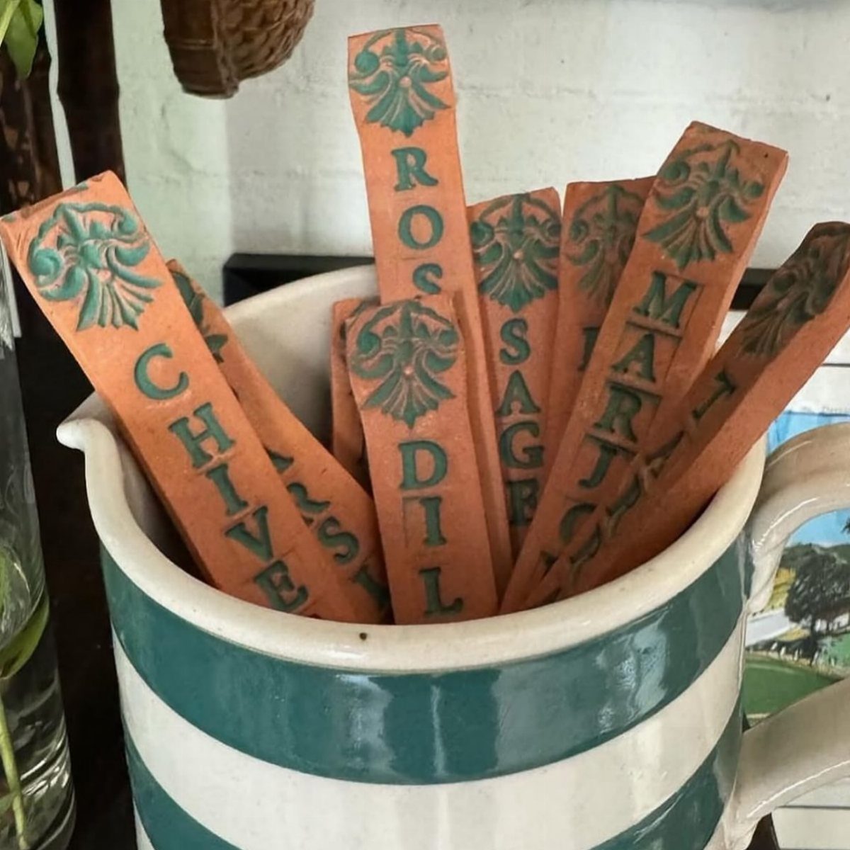 Terracotta herb garden labels with green lettering sitting inside a striped ceramic mug.