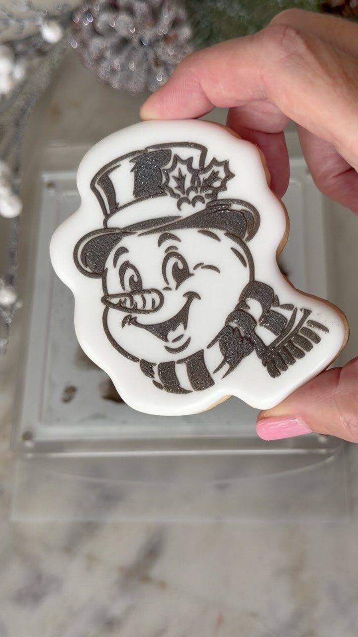 A hand holding a decorated snowman sugar cookie with black and white icing.