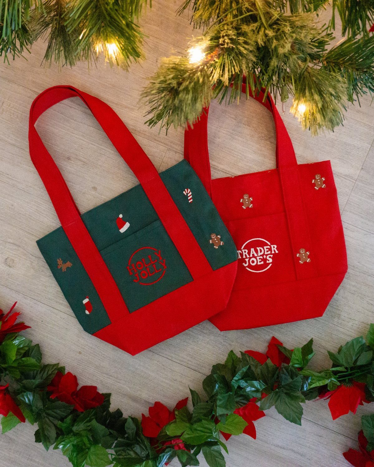 Two small red and green festive tote bags resting on a wooden surface with pine branches.