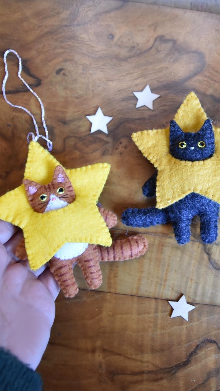 Two handmade felt cat ornaments with yellow star shapes resting on a wooden tabletop.