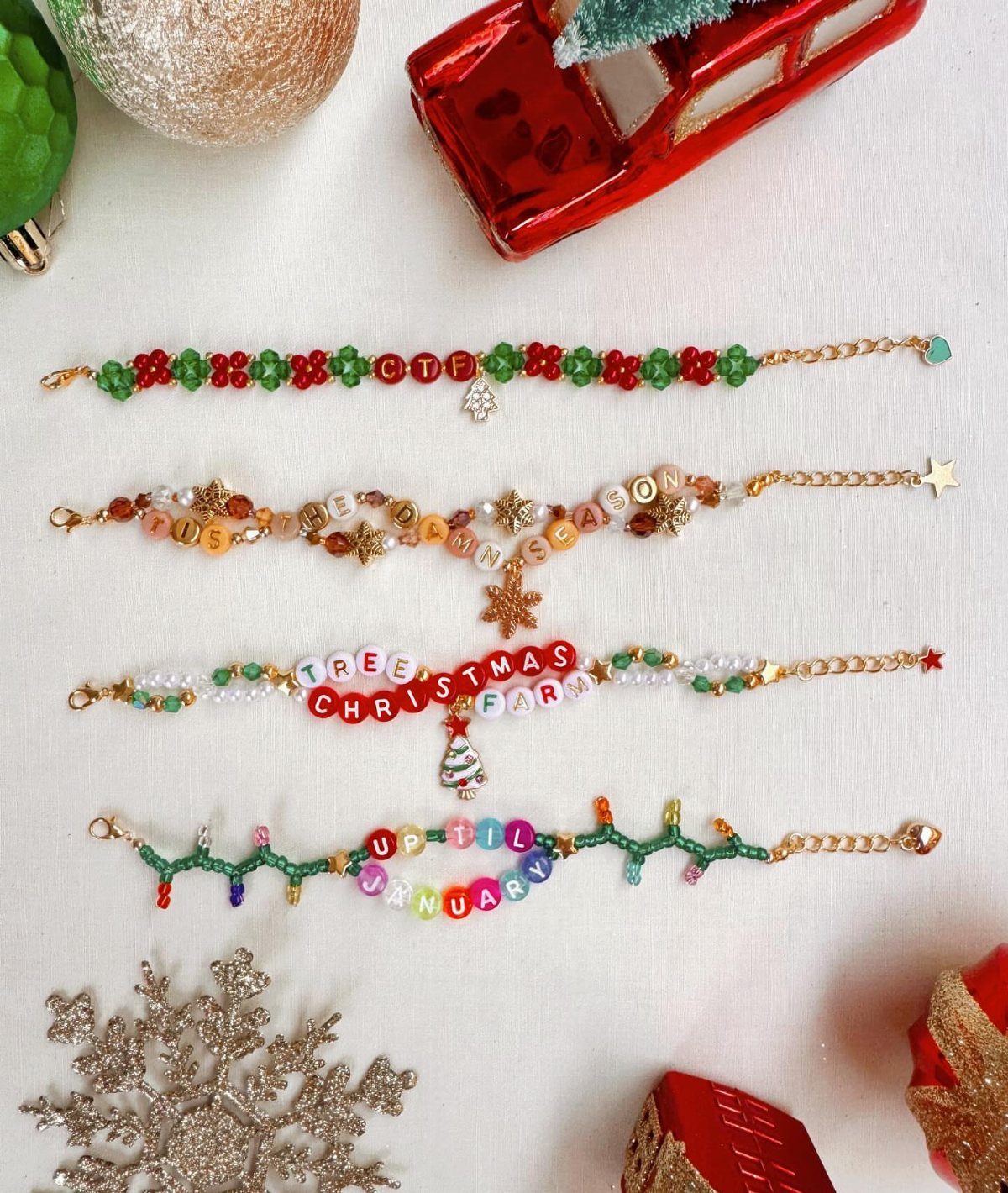 Four beaded friendship bracelets with letter beads spelling festive words on a white holiday background.