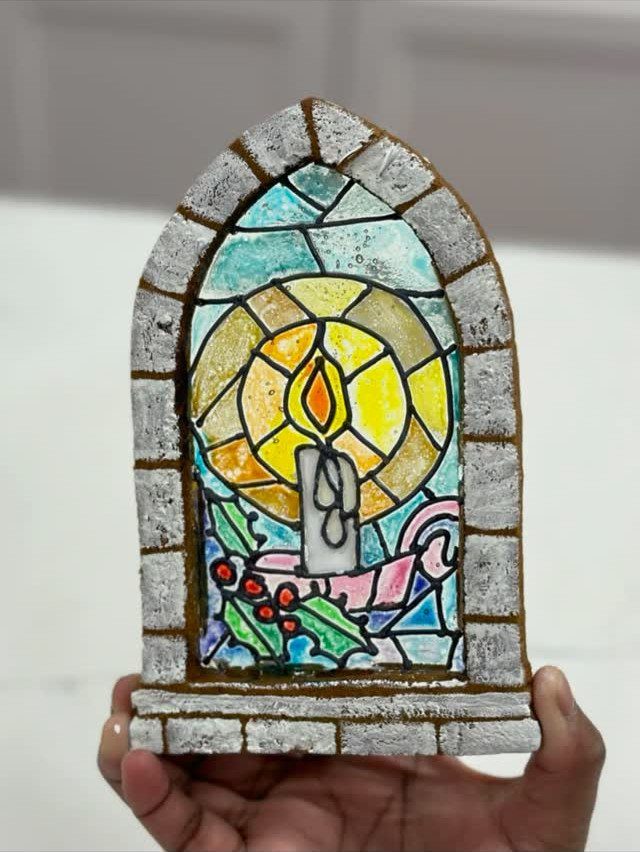 A person holding an arched gingerbread cookie decorated with colorful stained glass icing patterns.