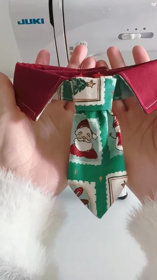 Hands holding a handmade green Christmas tie with Santa Claus patterns against a sewing machine.