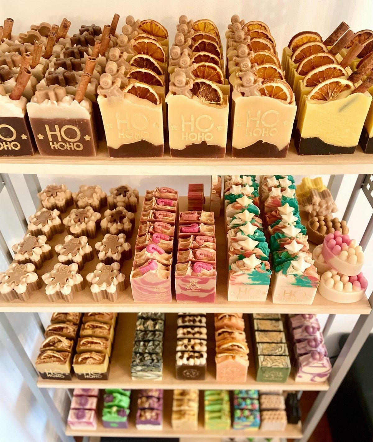 Various colorful handmade soap bars decorated with citrus and spices on white shelves.