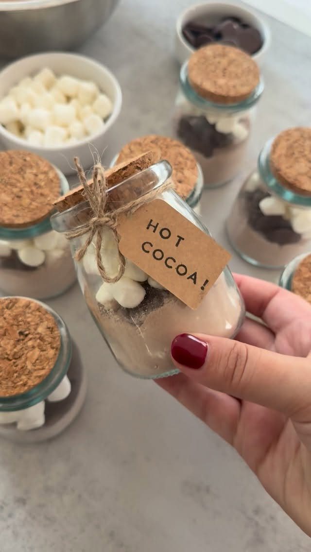 A hand holding a glass jar filled with layered hot cocoa mix and marshmallows.