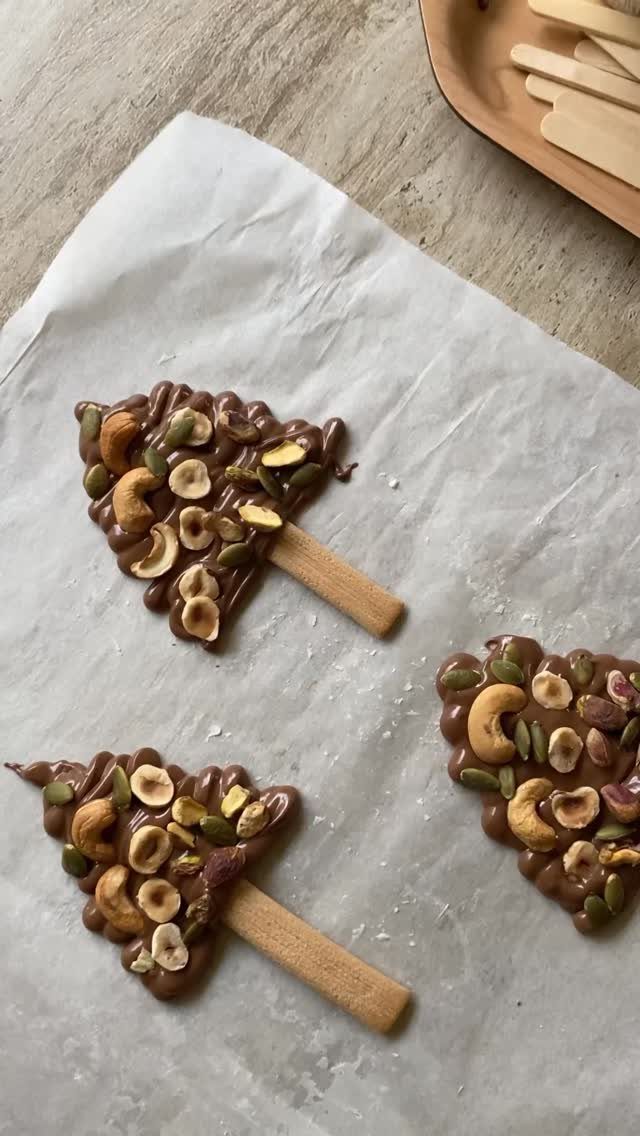 Three chocolate nut-covered treats shaped like Christmas trees on white parchment paper.