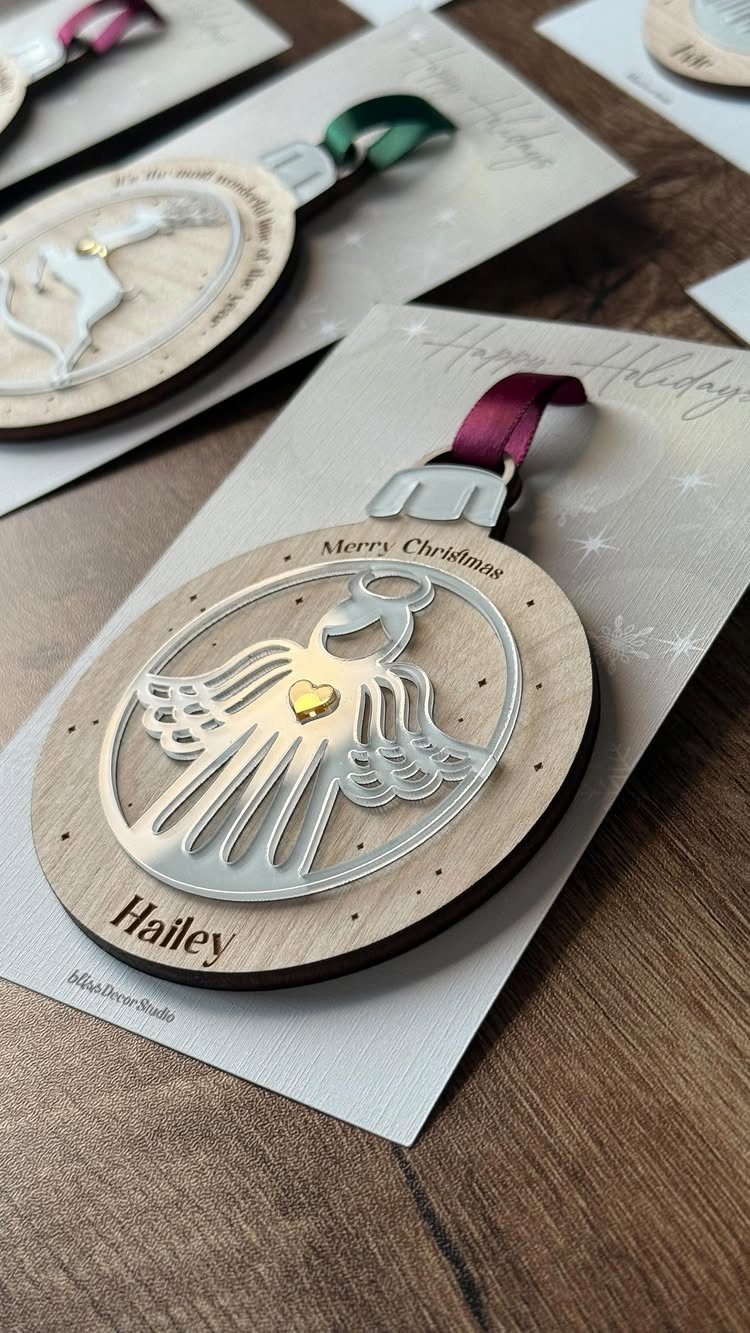 Wooden angel Christmas ornaments with personalized names resting on white gift cards.