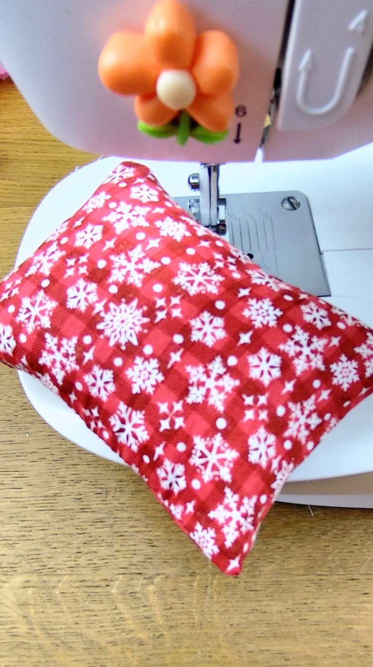 A small red pillow with white snowflakes resting on a white sewing machine.
