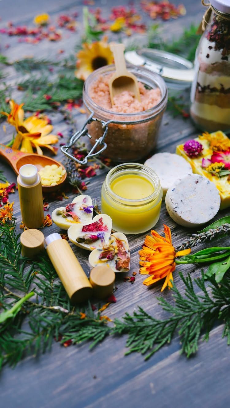 Handmade skincare products including sugar scrub, lip balm, and floral soaps on a wooden table.