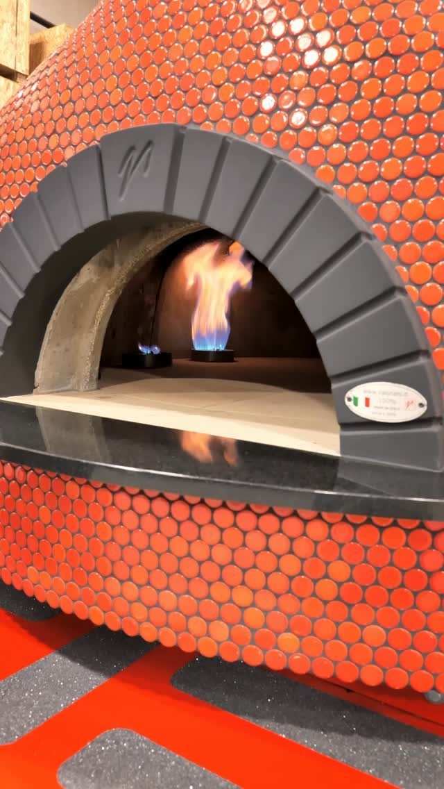 An orange mosaic tiled pizza oven with a glowing flame inside the arched opening.