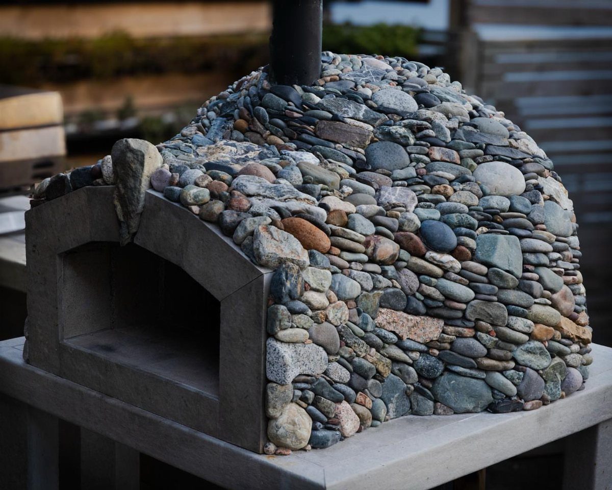A dome-shaped pizza oven built from various smooth, multi-colored river stones and pebbles.