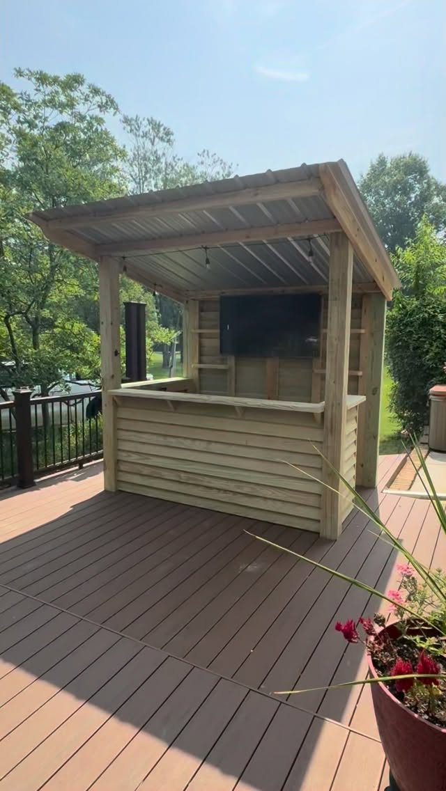 Deck with Patio Underneath: 5 Layouts That Actually Work 3 A wooden outdoor bar structure with a mounted television on a wooden deck.