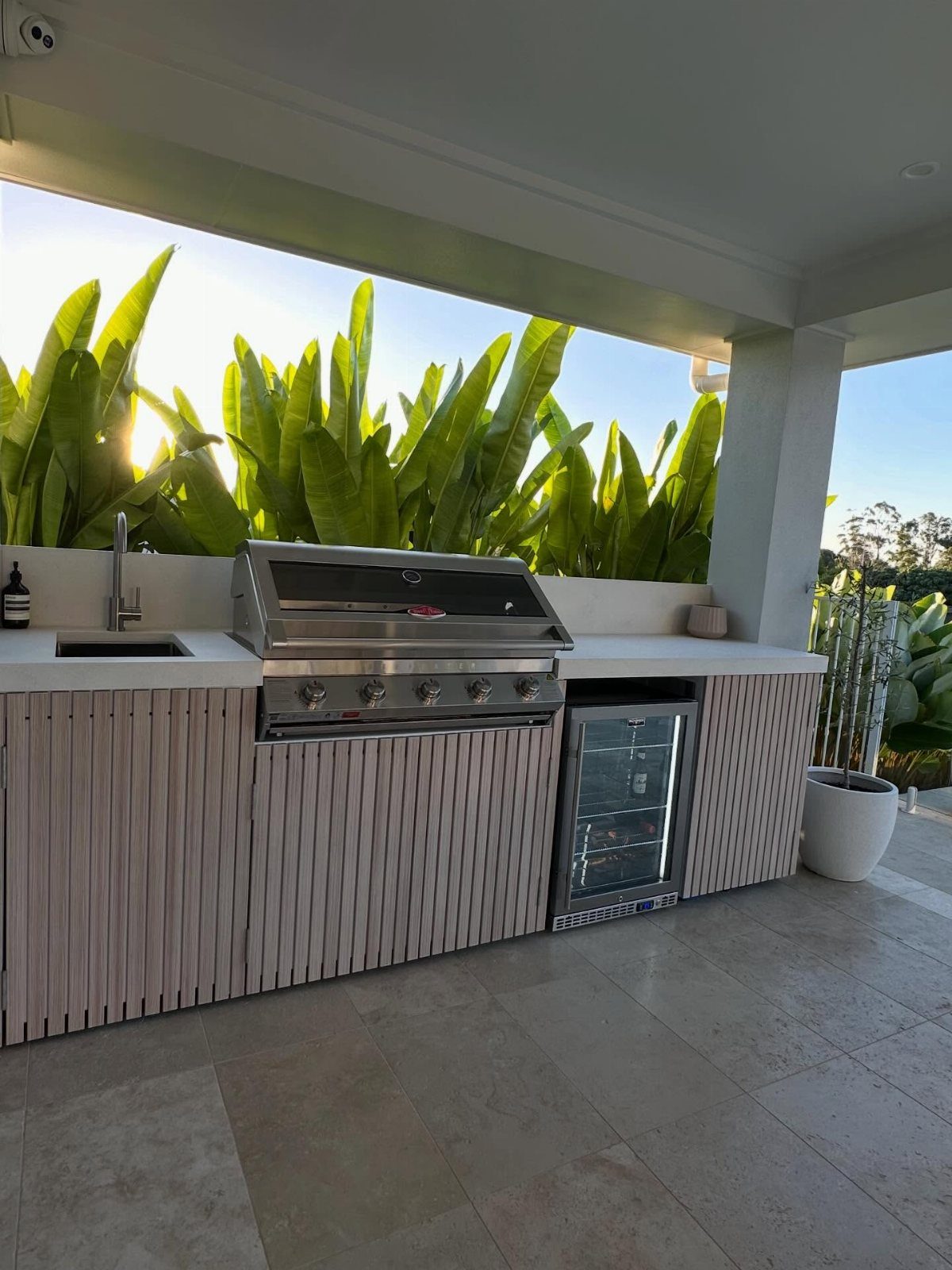 Deck with Patio Underneath: 5 Layouts That Actually Work 1 Stainless steel outdoor kitchen with a grill, sink, and beverage fridge under a white patio cover.