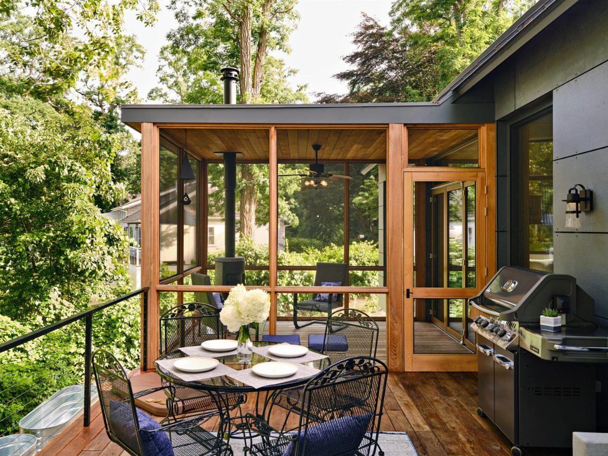 Deck with Patio Underneath: 5 Layouts That Actually Work 2 A wooden screened-in porch with a ceiling fan attached to a modern dark house and deck.
