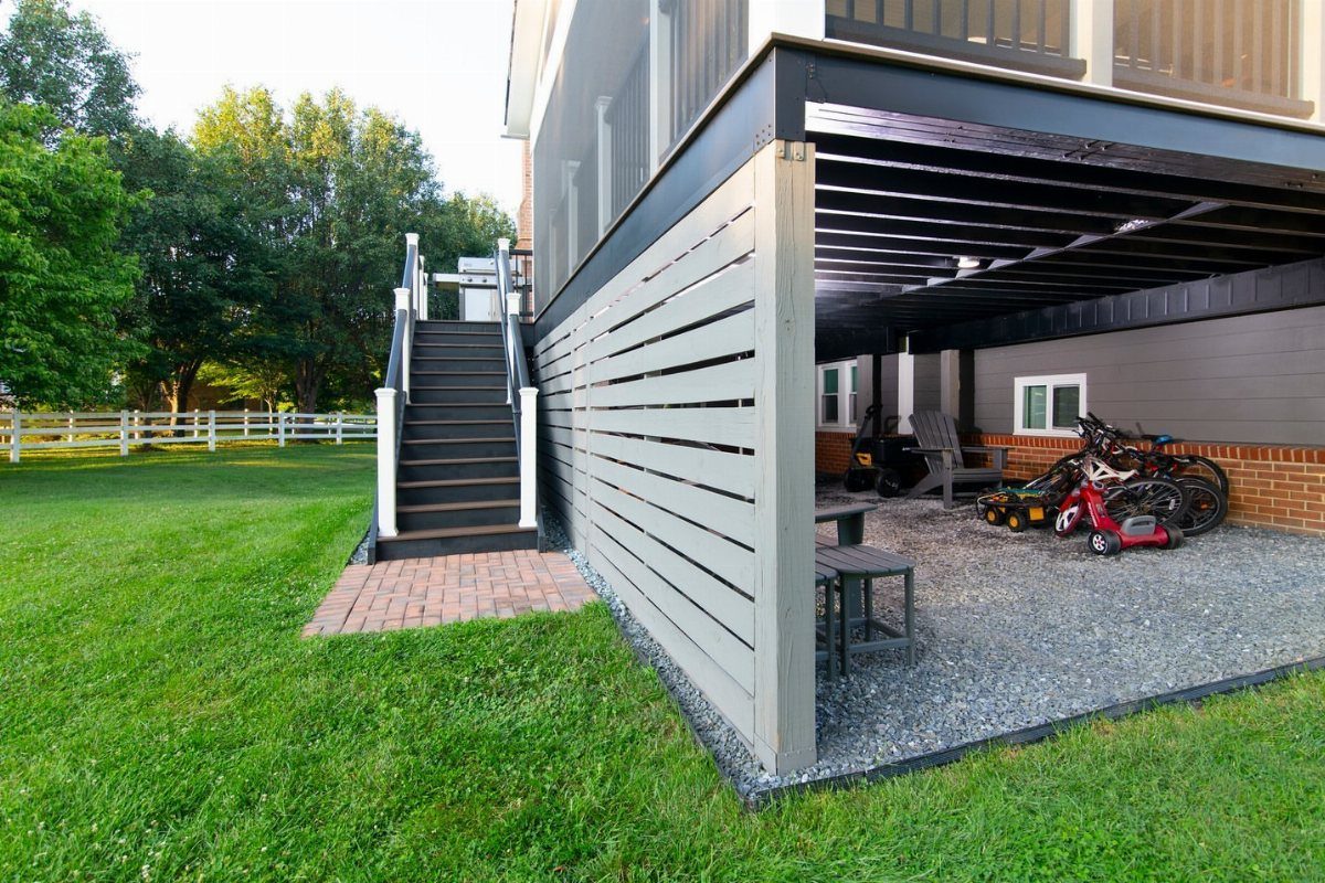 Deck with Patio Underneath: 5 Layouts That Actually Work 4 Children's bicycles and a tricycle parked on gravel under a grey wooden deck.