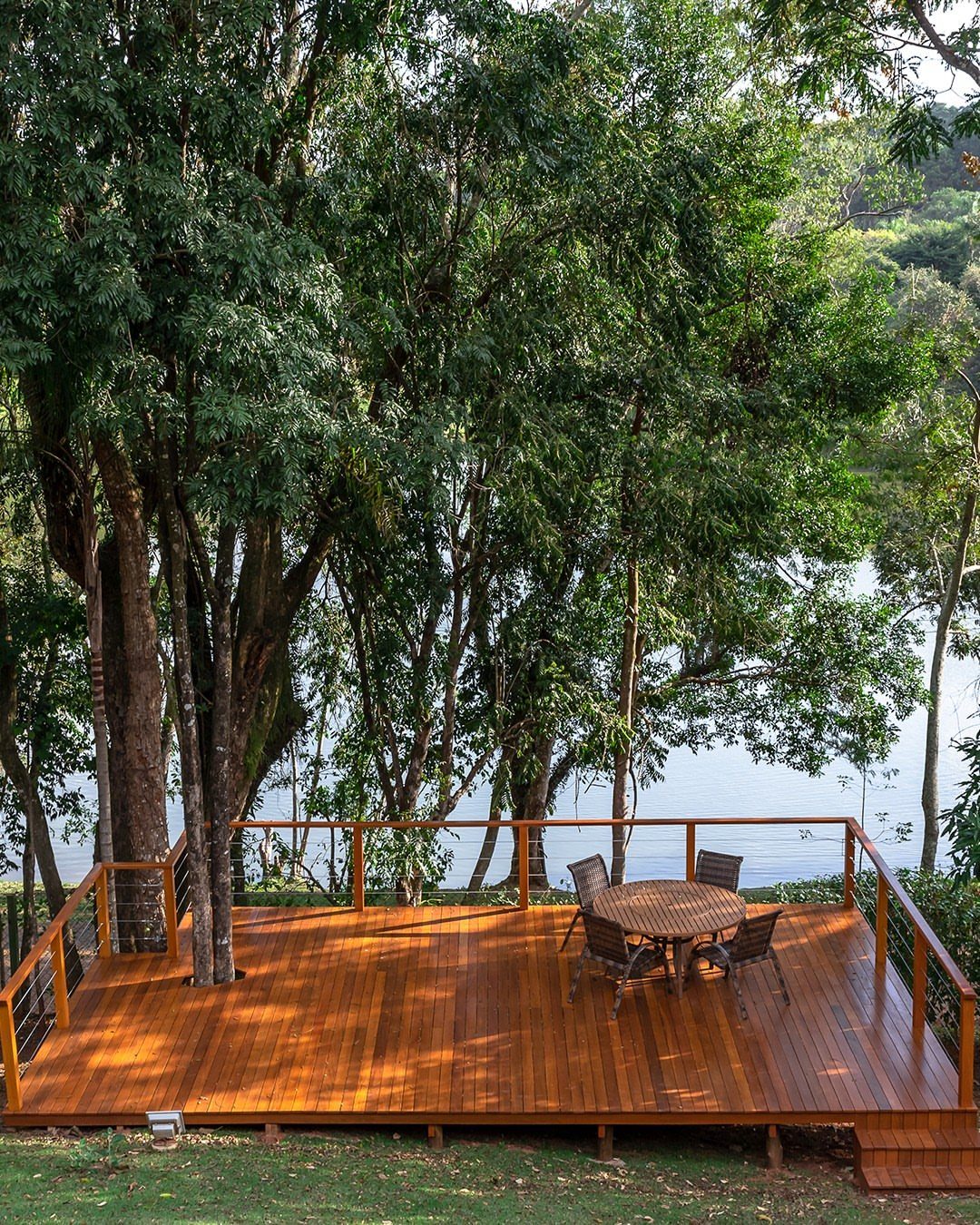 Decks de Madeira: 7 Ideas for Outdoor Living Spaces 5 Wooden deck with outdoor furniture built around a tree overlooking a lake.