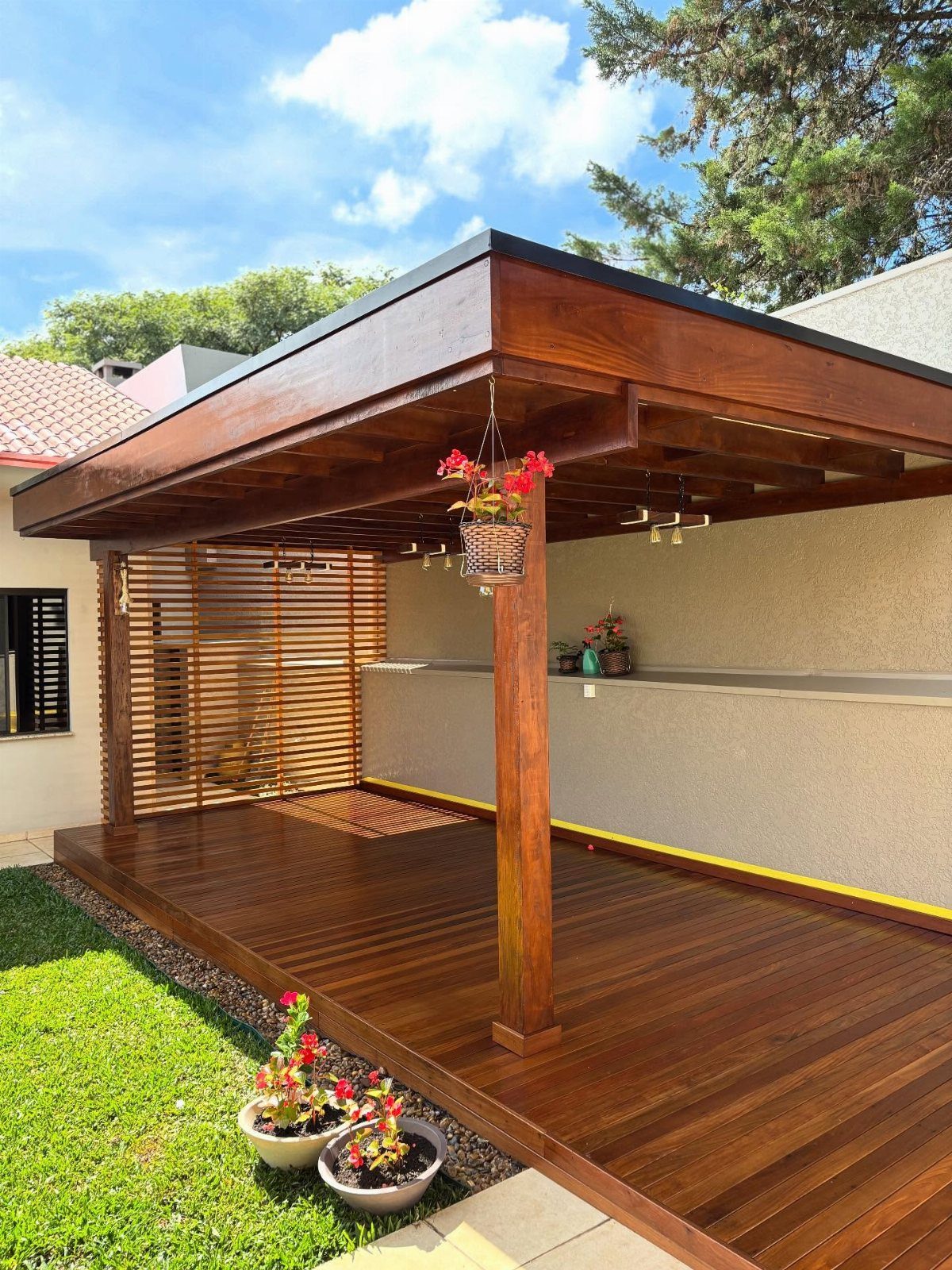 Decks de Madeira: 7 Ideas for Outdoor Living Spaces 3 A polished dark wood deck with a pergola structure and potted flowers in a garden.
